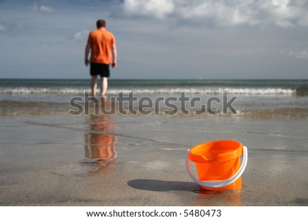 brigh orange sand bucket with water on the beach and boy on the background
