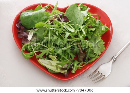 fresh leaf salad on red heart shape plate with fork on the table