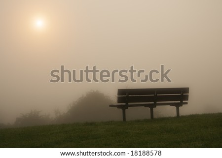 misty bench on a hill under the raising sun in the morning fog, soft focus