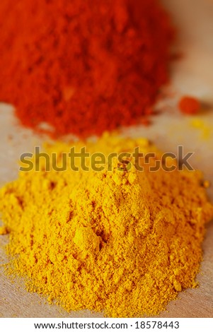 two color spices - pile of ground turmeric and paprika, shallow DOF, focus on top of the yellow pile.