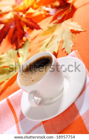 warm up in winter time!Cup of froth black coffee with  fall leaves and orange background, shallow DOF