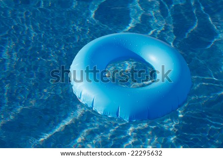 Blue life preserver or innertube floating  in a pool with waves reflecting in the summer sun