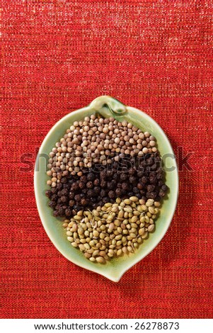 black coriander seeds , black peppercorn, white coriander in leaf bowl on red glitter backdrop, copy space
