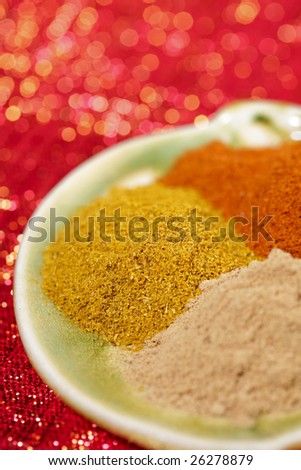 three piles of indian powder spice on plate,  Curry powder in focus, red glitter background, shallow DOF