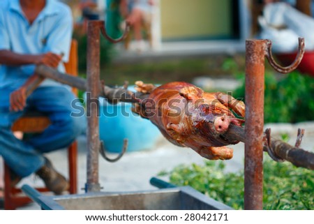 whole grill piglet pig on a roaster skewer outdoor with a man on background, shallow DOF