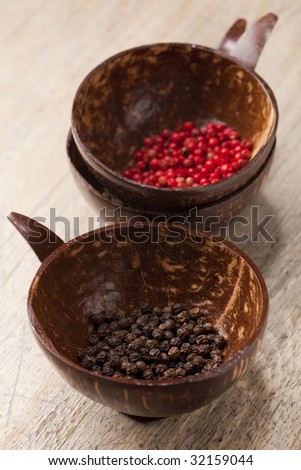 black and pink peppercorns in coconut bowls on old wooden table