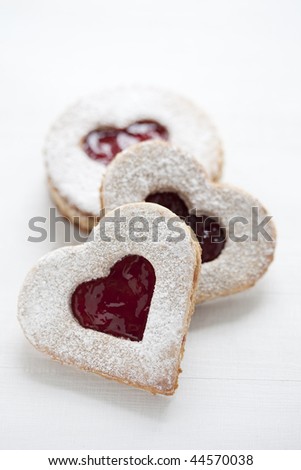 three linzer cookies with heart shape raspberry jam window, on white wood