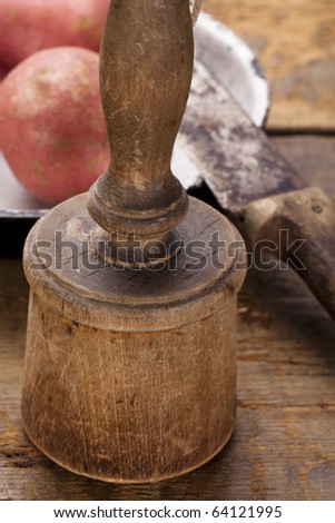 antique potato masher on  old wooden table with knife and potato, shallow dof