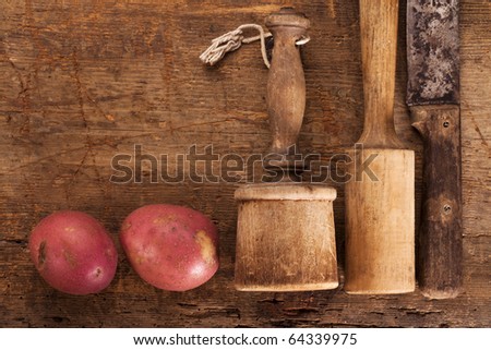 antique potato mashers and knife on  old wooden table with red  potatoes