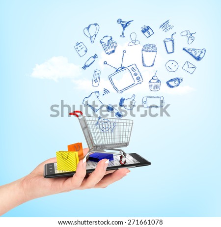On line shop concept. Female hand holding a phone on which stands empty shopping cart with falling drawing icons and colorful package. E-commerce.