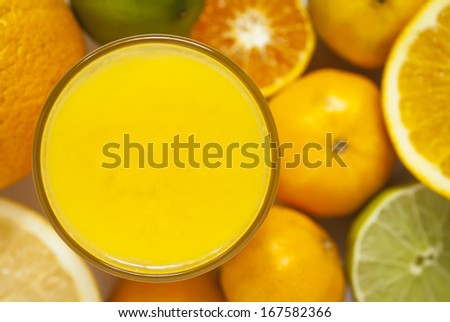 An overhead image of a glass with citrus juice, surrounded by citrus fruit.