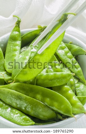 Freshly steamed snow peas in a white bowl with white chopsticks on a white cloth.
