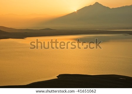 A bright yellow sun rises over a high desert lake.