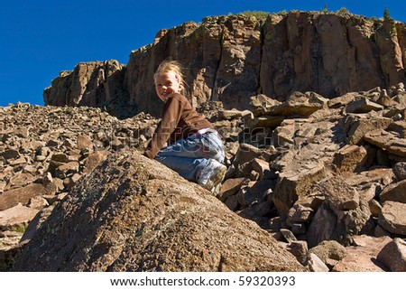 A young girl climbs scattered scree at the foot of a cliff.