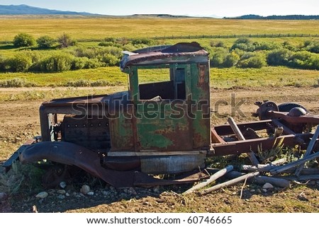 Old ranch truck decaying beside a dirt road.