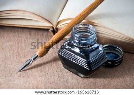 still life, opening vintage book on wooden table with quill pen and inkwell