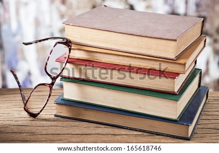 vintage books are stacked on wood plank with a reading glasses