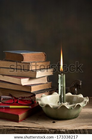 still life, Lighted candle and old books with glasses and pen on wood
