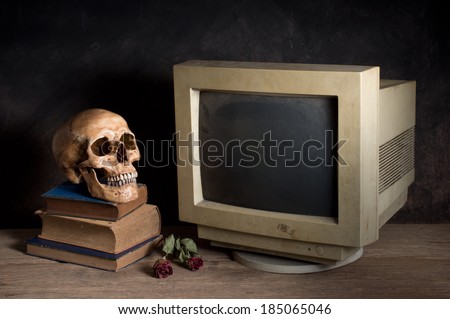 Still life photography, human skull with old computer monitor, old book and dry rose on old wood table
