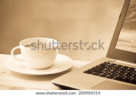 coffee cup with computer notebook on wood table with space for text in sepia color tone