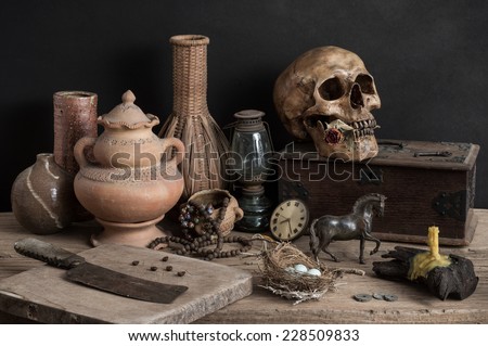 still life photography, skull with dry rose in the mouth and wooden box, candle, chopping block, clock, metal horse, egg, old knife, lantern, nest, pottery, rosary and wicker