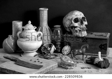 still life photography, skull with dry rose in the mouth and wooden box, candle, chopping block, clock, metal horse, egg, old knife, lamp, nest, pottery, rosary and wicker in black and white