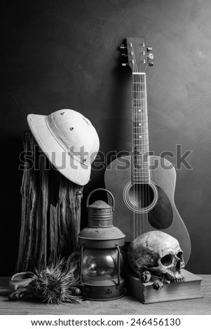 still life photography : hunter hat on tree stump, guitar, lantern, skull, old book, dry rose and tillandsia in country life concept in black and white