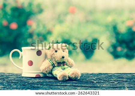 cute bear and mug on old wood table in blurred tree background in vintage color tone