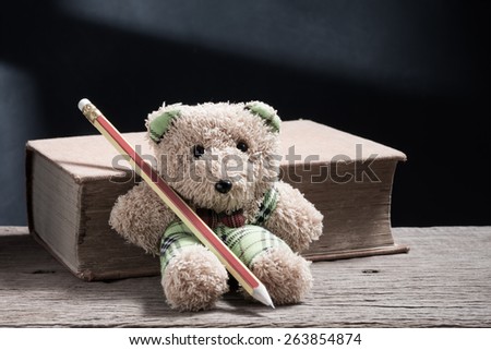 cute teddy bear have a pencil leaning at the old book on wood in vintage color tone