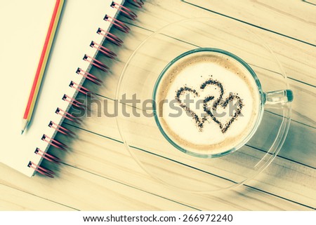 latte art : cup of coffee with two heart shape symbol and pencil on binder notebook in vintage color tone