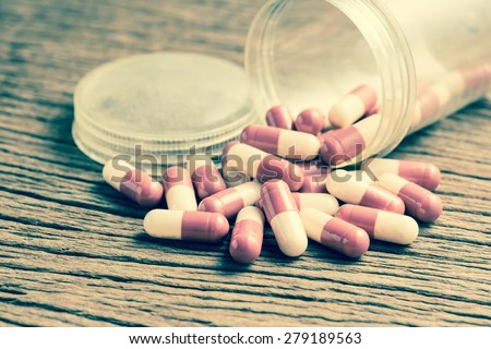 pills capsules with old plastic bottle on wood  in cross process vintage color tone