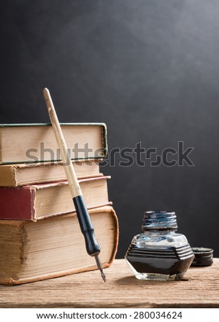 still life photography : old inkwell and dip pen with old books on art dark background