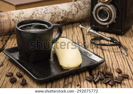 still life photography : espresso coffee cup and banana cake in saucer with coffee beans on old wood and camera, shutter release cable and map at background