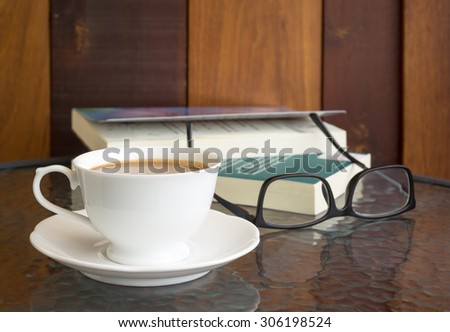 coffee cup on glass table with eyeglasses, Fiction book and wooden wall background