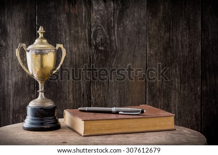 still life photography : old trophy, book and pen on old wooden table with space of old wood background