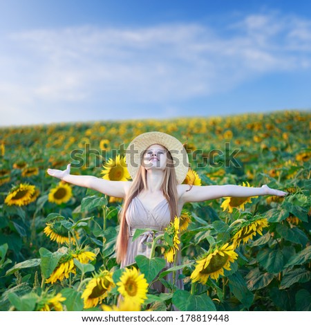 Beautiful happy young woman on the sunflower field under summer sky with freedom emotions