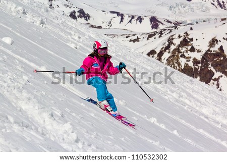 Little girl skier rides in the soft snow on a steep hill, on a sunny day