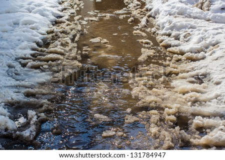 Flow of water with lumps snow melts on the road in the city