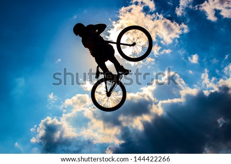 Silhouette of a cyclist flying in background the sun and blue sky with clouds