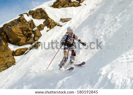 Female skier on a very steep off-piste in the background of rocks. In sunny weather.