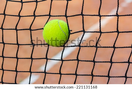 Yellow-green tennis ball stuck in the grid on red clay courts