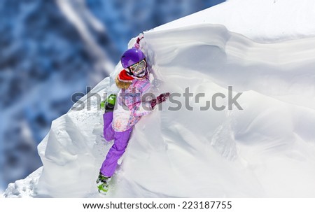 Little Girl in bright ski clothes climbs a snow cornice in the mountains on a sunny day
