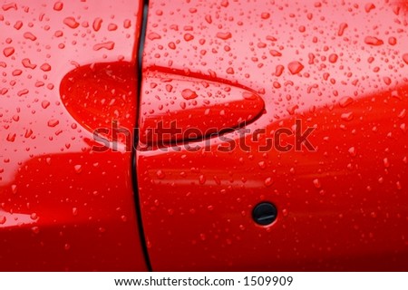 A closeup shot of a red sports car door with rain spots
