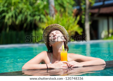 beautiful woman in straw hat with fresh juice in luxury pool