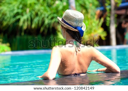 back view of beautiful woman in straw hat in luxury pool