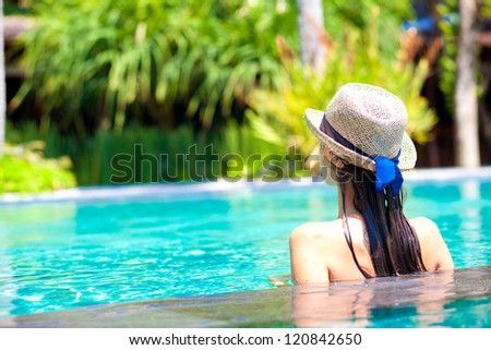 back view of beautiful woman in straw hat in luxury pool