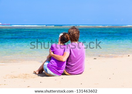 back view of young happy couple sitting on tropical beach. honeymoon concept