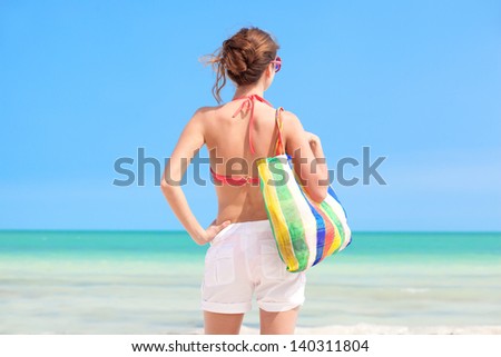 back view of woman in straw hat and bikini with beach bag