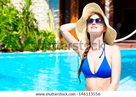 long haired beautiful woman in straw hat and sunglasses in luxury pool