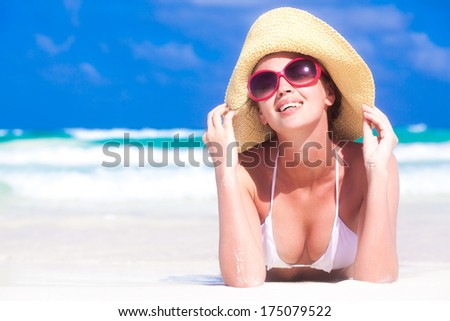 front view of beautiful young woman in sunglasses and straw hat lying on beach enjoying the sun